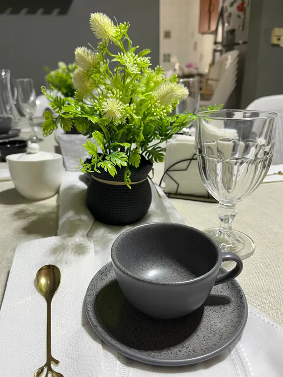 Mesa encanto: taza gris sobre plato, cucharita dorada en forma de hoja y planta en maceta negra