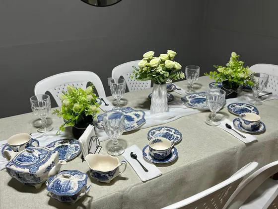 Mesa con vajilla de loza azul y blanca, rosas blancas, plantas y copas de cristal sobre mantel de lino