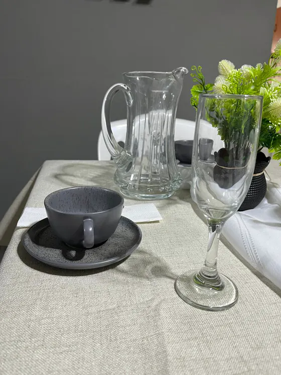 Taza gris sobre plato, jarra de vidrio y copa de champagne