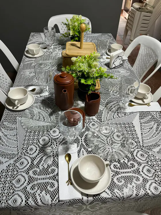 Mesa vista desde arriba con mantel de encaje, juego de café marrón, tazas crema, platos de vidrio y cucharitas doradas