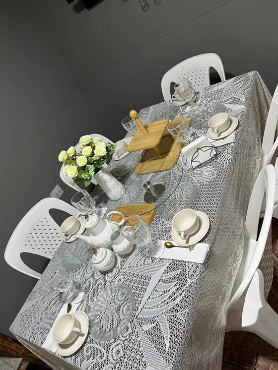 Mesa con mantel de encaje, juego de té floreado, posatortas de bambú y rosas blancas