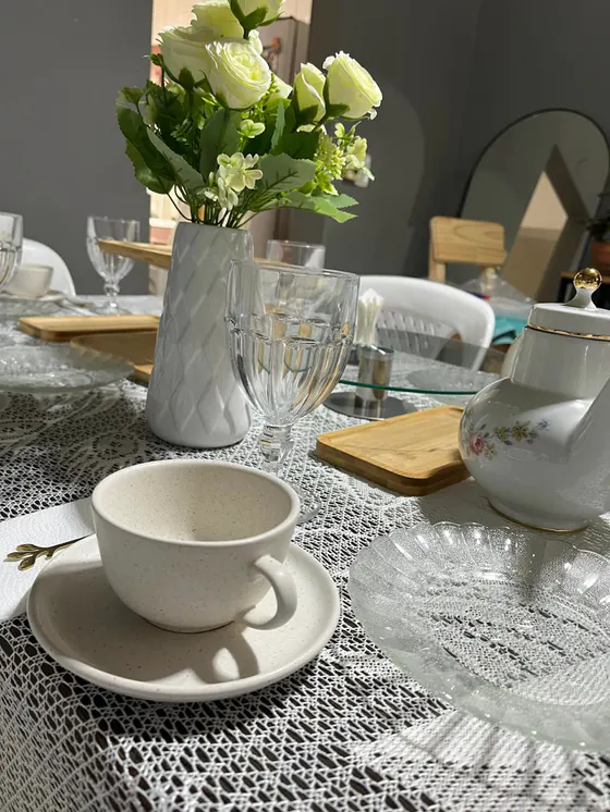 Taza crema con cucharita dorada, plato de vidrio y tetera floreada